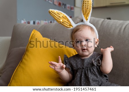 portrait of little baby girl in gray dress and golden bunny ears siting on sofa at home