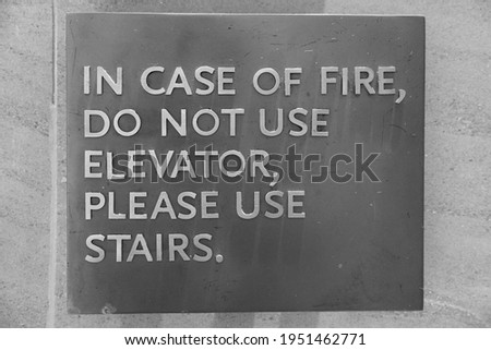 A sign that says, In Case Of Fire, Do Not Use Elevator, Please Use Stairs, which direct people of what to do in case of an fire emergency. Black and White Photo. 