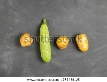 Ripe juicy zucchini with raw early potato tubers on chalk board