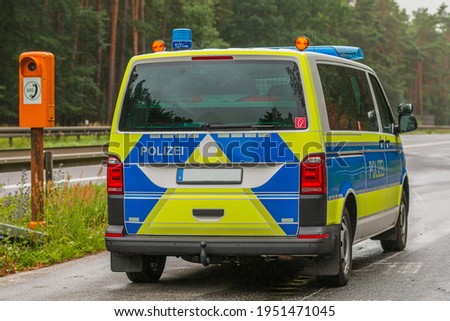 Police car in an emergency bay on a motorway in the state of Brandenburg. Emergency telephone on the roadside. two-lane highway with asphalt surface in rainy weather. Guard rail and trees
