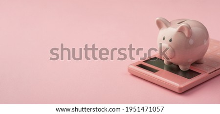 Closeup photo of piggy bank on pink calculator isolated pink background with copyspace
