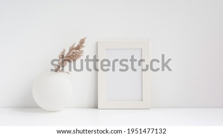 White frame mockup with spherical vase and dry grass on a white table
