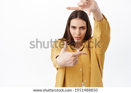 Creative and passionate woman searching perfect angle, looking through hand frames camera gesture and determined pensive look, creating something, standing over white background