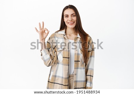 Thats fine. Smiling young woman shows okay sign and nods in approval, looks pleased, satisfied with good quality, praise nice work, excellent choice, stands over white background