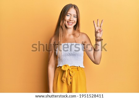 Beautiful young blonde woman wearing casual summer clothes showing and pointing up with fingers number three while smiling confident and happy. 