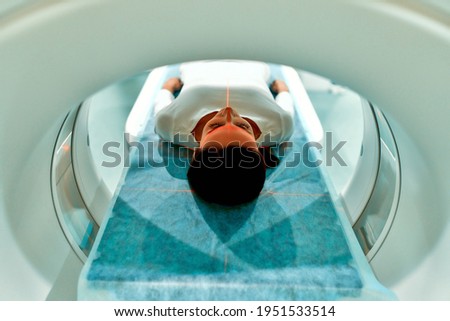 Portrait of a patient lying on CT or MRI, the bed moves inside the machine, scanning her body and brain. In a medical laboratory with high-tech equipment. Royalty-Free Stock Photo #1951533514