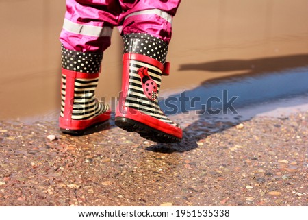 Legs of a child in striped red and black rubber boots  boots running near the puddle. Spring, puddles and pure happiness. Copy space, stock photo