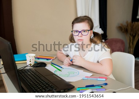 Teenager girl with Down syndrome drawing planet Earth for online lessons. Distance learning by video call on laptop. E-learning and creative development for kids with special needs concept