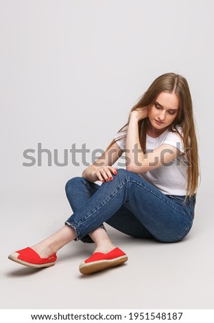 young beautiful woman in a white t-shirt and jeans on a white background. Young woman sit on white background. Photo concept for advertisements of clothes and shoes.