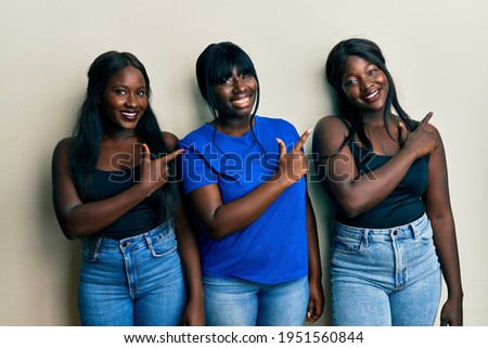Three young african american friends wearing casual clothes smiling cheerful pointing with hand and finger up to the side 