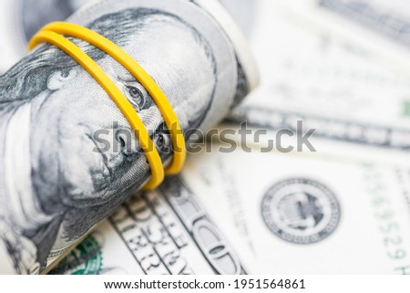 A roll of one hundred dollar bills and tied with an elastic band on the background of dollar bills.