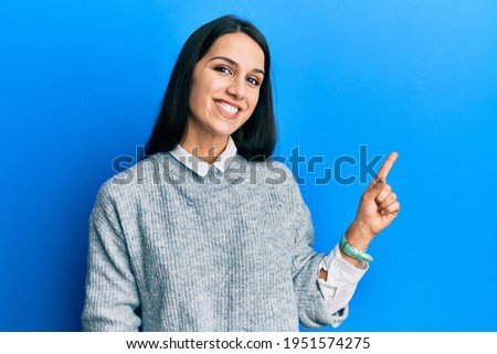 Young hispanic woman wearing casual clothes with a big smile on face, pointing with hand finger to the side looking at the camera. 