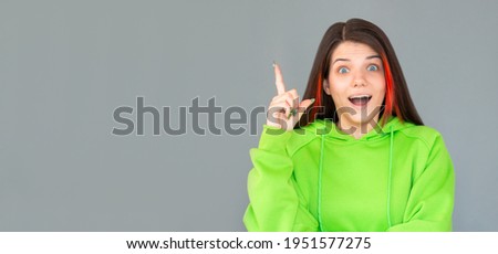Surprised brunette woman with arm on hip having idea and looking at th camera over gray background