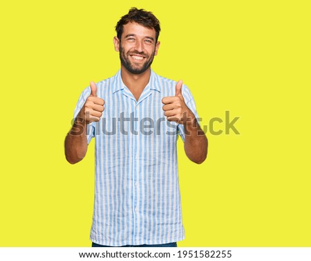Handsome young man with beard wearing casual fresh shirt success sign doing positive gesture with hand, thumbs up smiling and happy. cheerful expression and winner gesture. 
