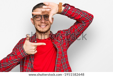 Hispanic young man wearing casual clothes smiling making frame with hands and fingers with happy face. creativity and photography concept. 