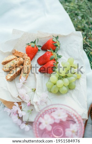 Spring picnic in nature. A glass of pink champagne with sakura flowers, a wicker bag, a hat, Italian.