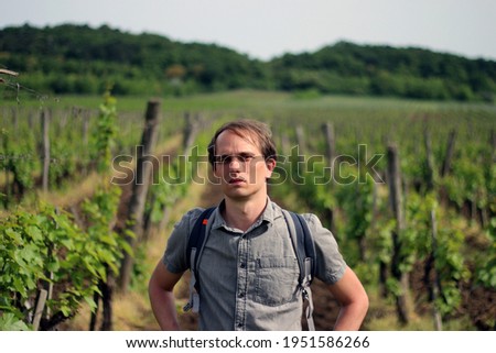 A handsome young caucasian man with light hair against the background of the grape field vineyard. Male person in natural landscape of Tihany in Hungary. Sunny weather and great place for agritourism.