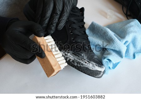 Man is cleaning sneakers in a workshop. Shoe shine service. The shoemaker prepares the shoes for the season. Shoe brush close-up. Shoe care with a special product Royalty-Free Stock Photo #1951603882
