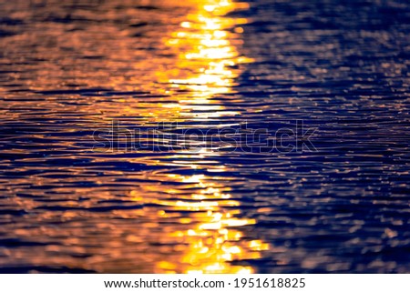 Sea waves texture with sunset or sunrise light reflecting on the water. Sunbeams illuminate the blue ocean water with warm orange light. Closeup view. Artistic and creative nature background.