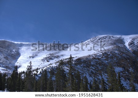 This is a landscape picture of snow covered mountains, lined with green trees.