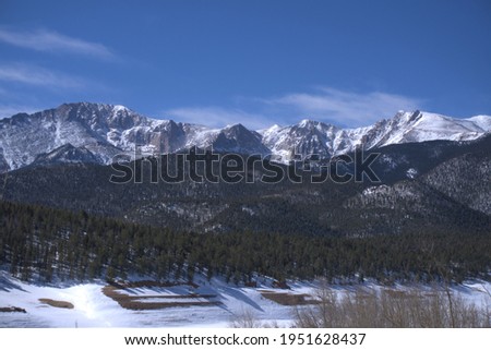 This is a landscape picture of snow covered mountains, lined with green trees.