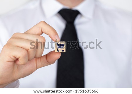 Businessman shows a wooden cube with shopping cart icon. Online shopping or add to basket concept.
