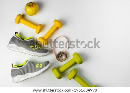 Gym and workout, 
sports shoes, sneakers, Healthy lifestyle concept foto. Flat lay of sport. Athlete's set with centimeter tape, green apple and dumbbells on a grey background Royalty-Free Stock Photo #1951634998