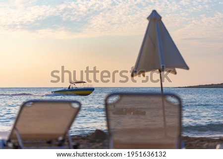 Evening at the sea in Cyprus. Sun loungers and an umbrella on the background of the sea and a boat.