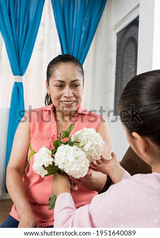 mother smiling as she receives flowers from her young daughter for mother's day