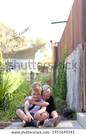 Portrait image of two little boys sitting in pretty garden setting sharing a loving hug with copy space