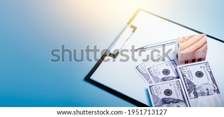 Wooden Small house, stacks of dollar bills and document file on blue background. Mortgage House loan concept