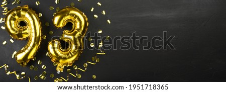golden foil balloon number ninety three. Birthday or anniversary card with the inscription 93. Black concrete background. Anniversary celebration. Banner. Copy space