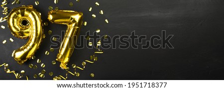 golden foil balloon number ninety seven. Birthday or anniversary card with the inscription 97. Black concrete background. Anniversary celebration. Banner. Copy space