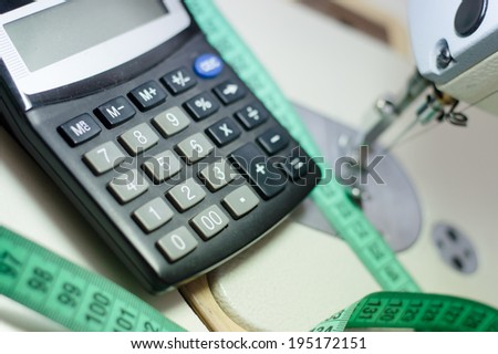 close up picture of calculator at white  sewing machine and green measuring tape