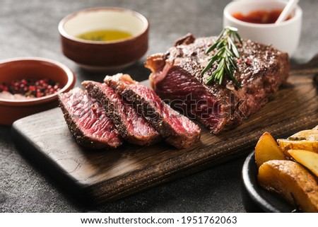 Sliced grilled meat steak New York Striploin with sauce and potato on wooden board on grey background Royalty-Free Stock Photo #1951762063