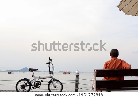 Man sitting alone on a wooden bench, looking at the sea next to the bicycle.