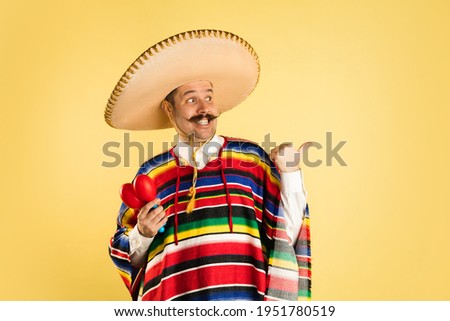 Portrait of man in bright garment and sombrero isolated over yellow background Royalty-Free Stock Photo #1951780519