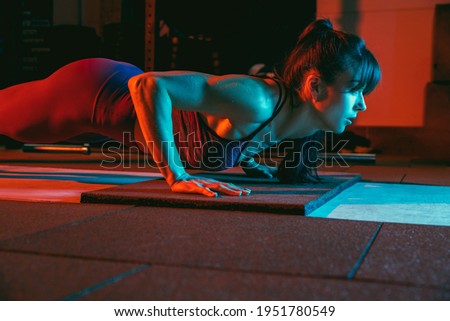 Young athletic woman, fitness instructor training in gym in mixed neon light.