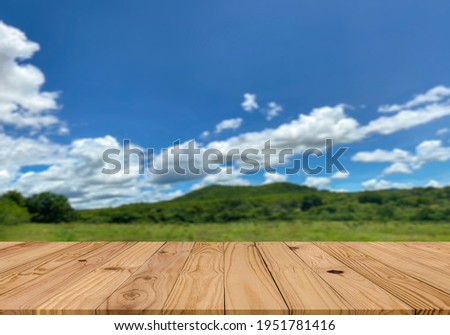 Empty perspective brown plank wooden board mock up display as shelf or table with blurred background sunshine blue sky and white clouds on the green mountain and  grass field.