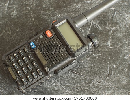 A black portable analog walkie-talkie on a dark concrete background. Close-up