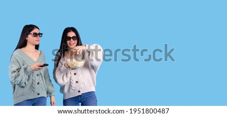 Banner, long format on blue background. Cute sisters, twins, girls wearing 3d glasses watching movie in evening, eating popcorn. Cinema show. Side copy space for ads. High quality photo