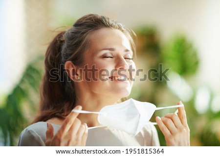 coronavirus pandemic. relaxed middle aged woman in grey blouse taking off ffp2 mask in the modern house. Royalty-Free Stock Photo #1951815364