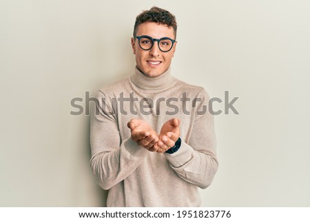 Hispanic young man wearing casual turtleneck sweater smiling with hands palms together receiving or giving gesture. hold and protection 