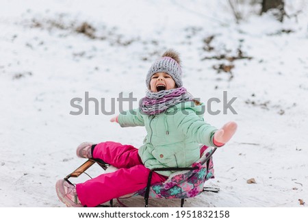A little girl, a child, dressed in warm clothes, in the cold winter sleds down the hill on a fresh white snow. Emotions, photography.