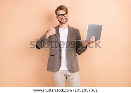 Photo of optimistic nice blond hair man hold laptop show thumb up wear spectacles grey jacket isolated on beige background
