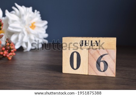 July 6, Date cover design with calendar cube and white Paeonia flower on wooden table and blue background.