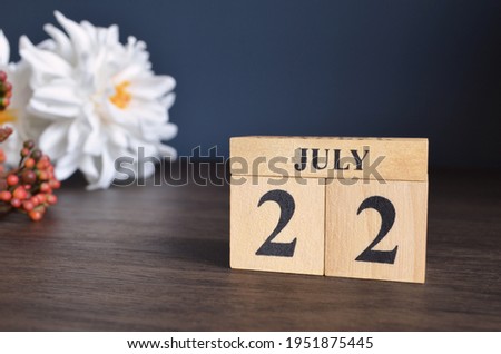 July 22, Date cover design with calendar cube and white Paeonia flower on wooden table and blue background.