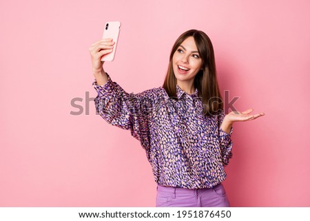 Photo portrait of woman taking selfie holding phone in one hand isolated on pastel pink colored background with blank space