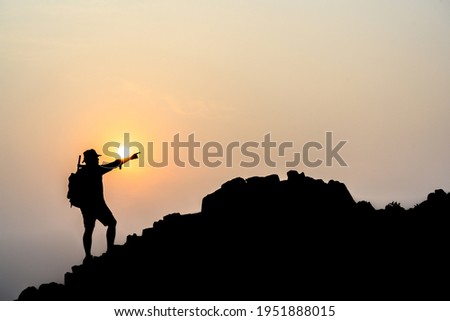Silhouette of young male tourists Stand and watch the beautiful sunset on top of the mountain with your backpack. Royalty-Free Stock Photo #1951888015