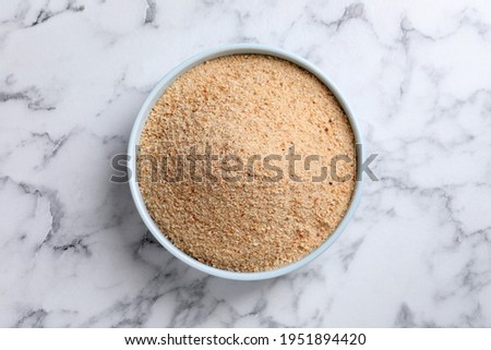 Fresh breadcrumbs in bowl on white marble table, top view
